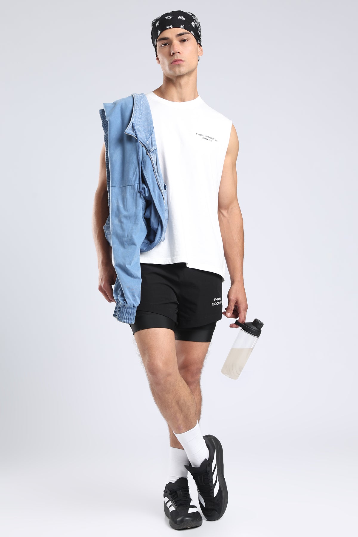 Model wearing the white Hybrid Athletes Tank with black training shorts and a blue jacket