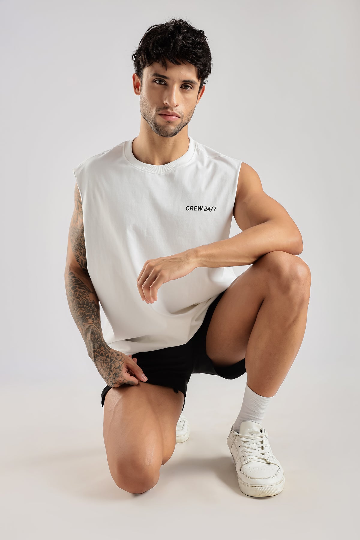 Model wearing the white Push Pull Tank with Crew 24/7 chest branding while seated