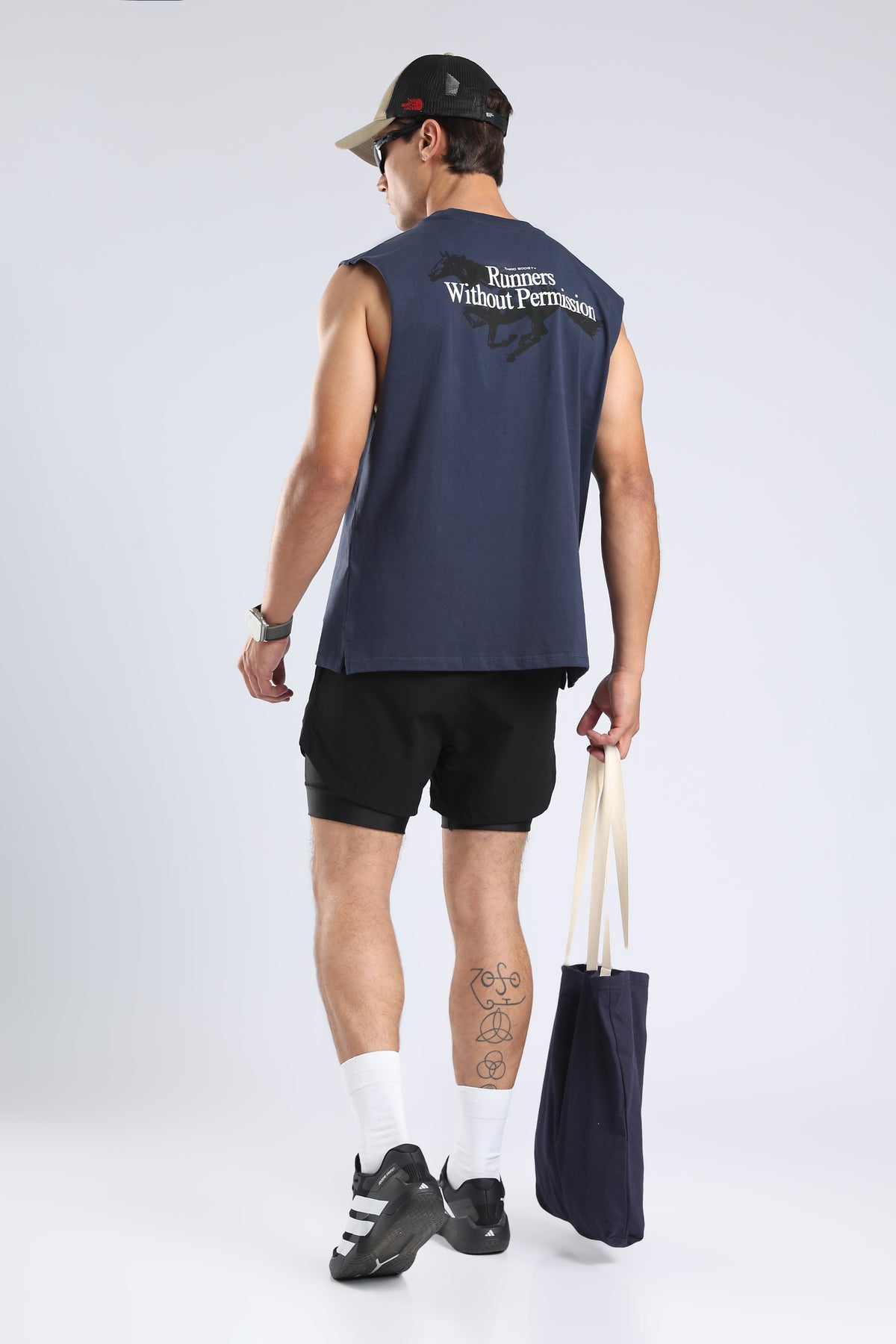 Model wearing the Iron Blue tank with the Runners Without Permission back graphic and a tote bag