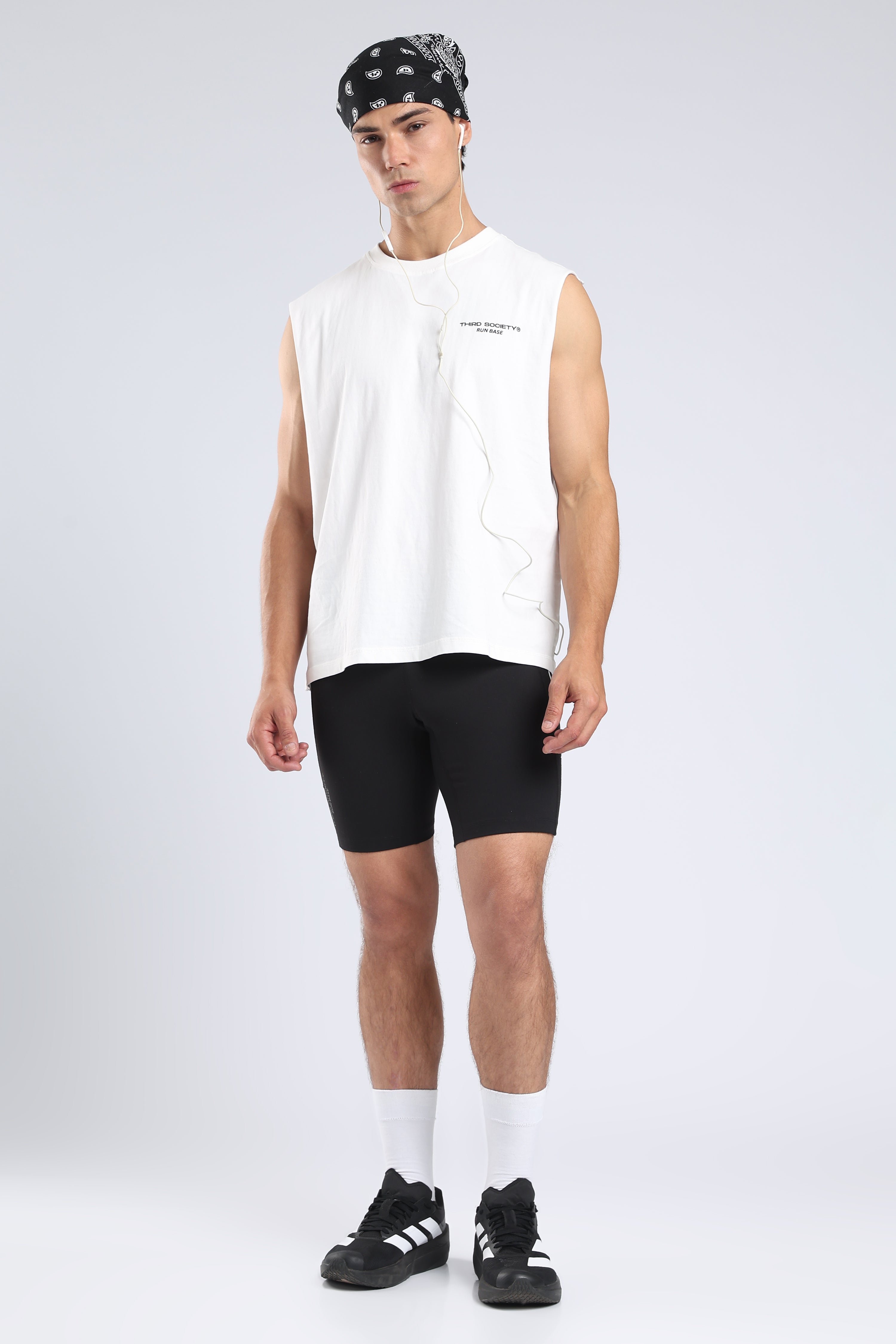 Model styling the white tank with black running shorts and trainers