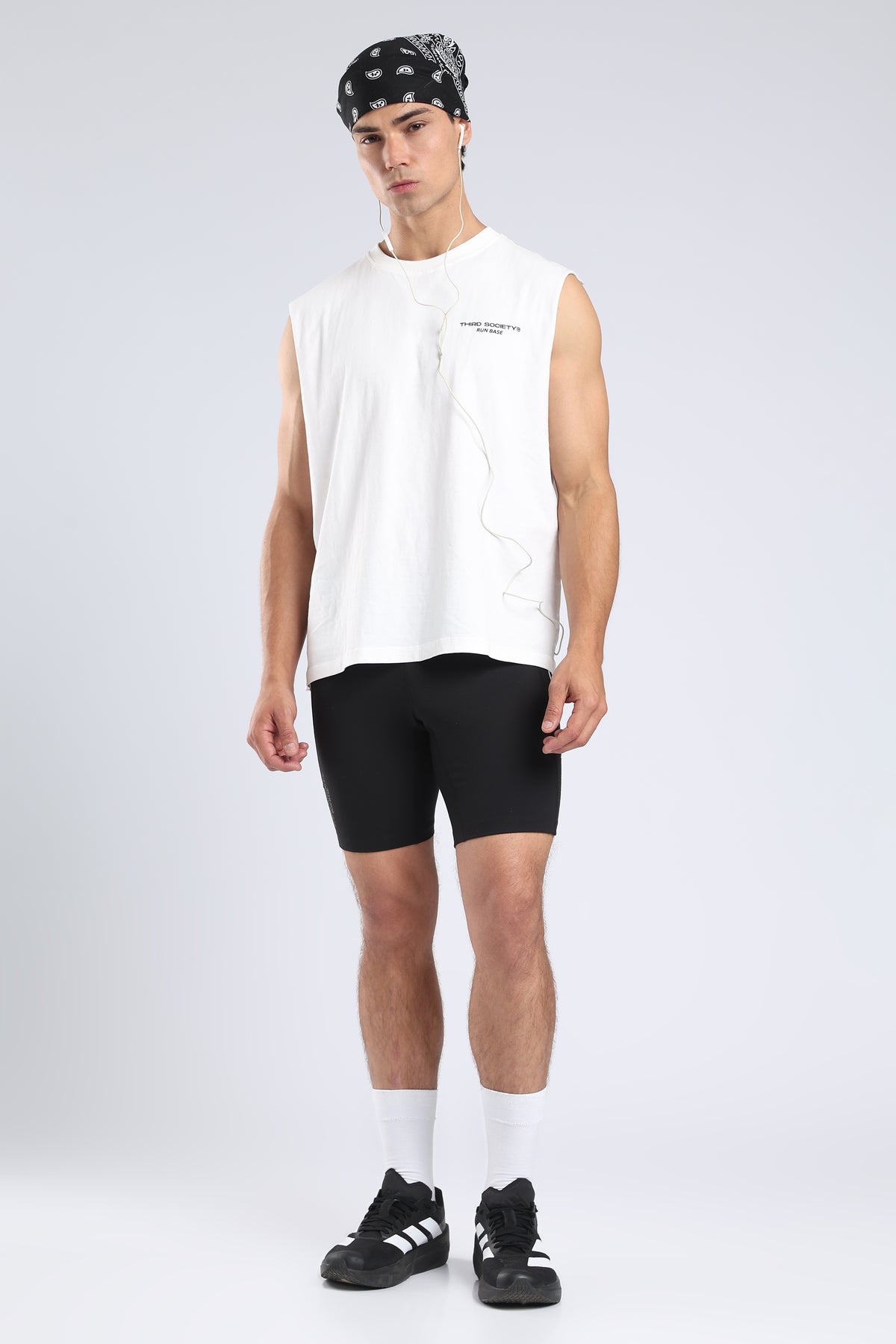 Model styling the white tank with black running shorts and trainers